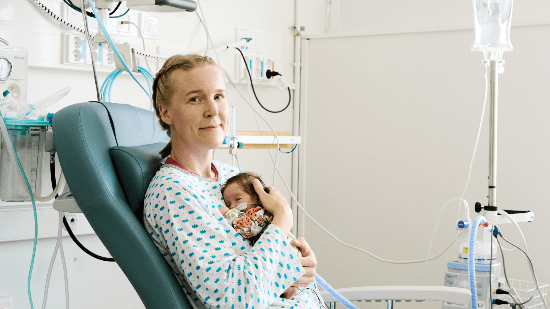 HelsinkiMission vapaaehtoinen sylikaveri istuu sairaalaosaston tuolilla ja pitelee sylissään pientä vauvaa.