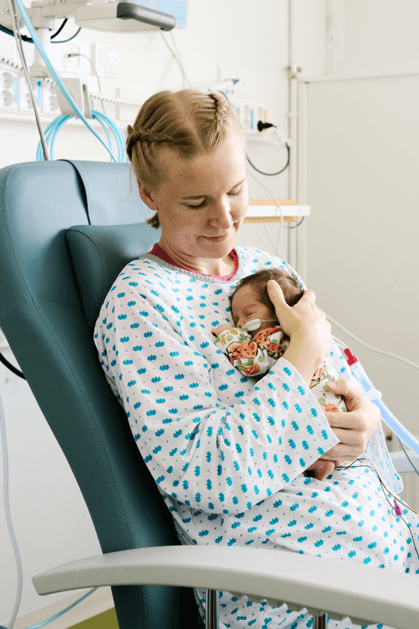 HelsinkiMission vapaaehtoinen perhekaveri katsoo pientä vauvaa, jota pitelee sylissään rinnan päällä.
